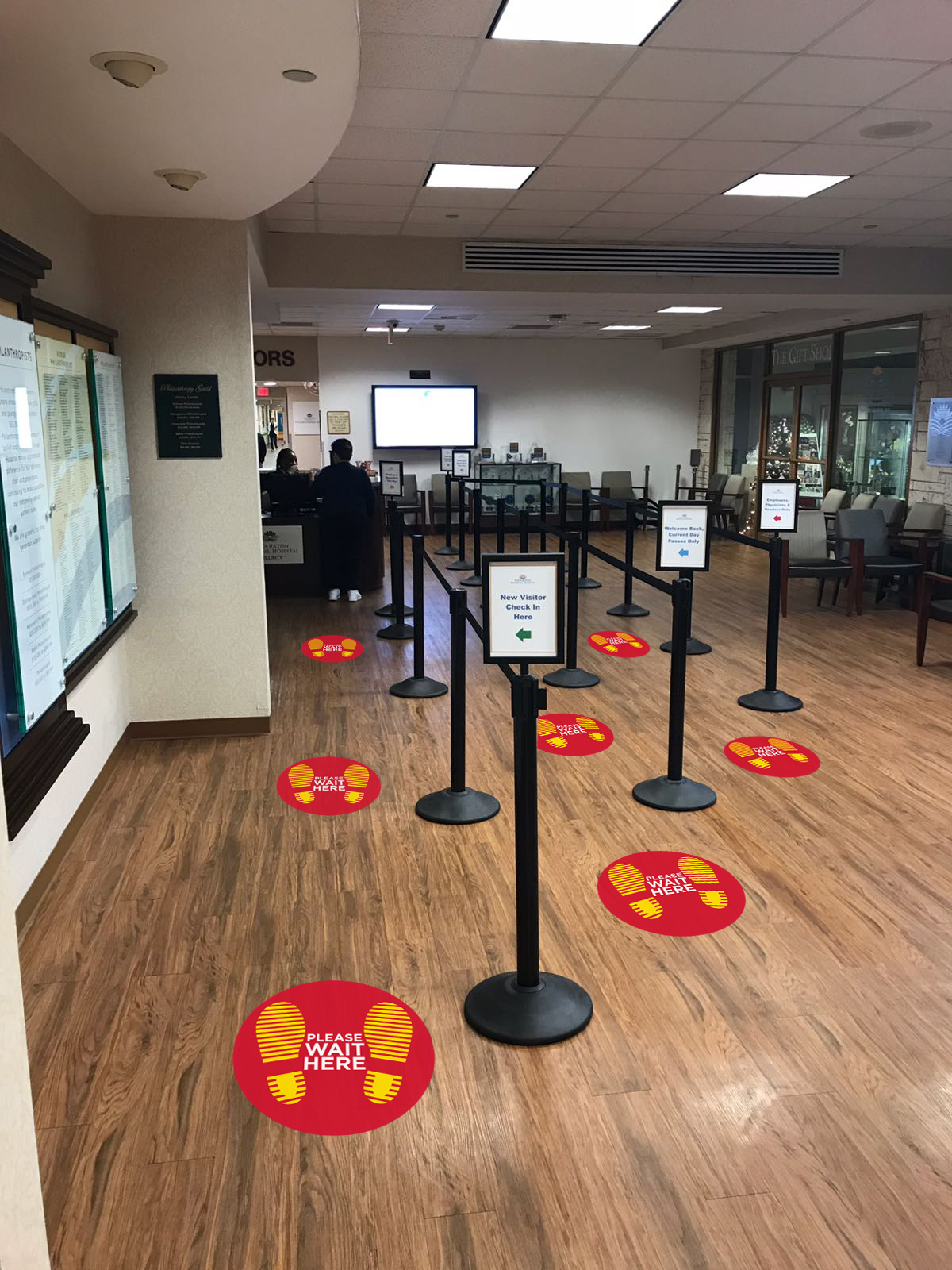A waiting area with a wooden floor features a row of black stanchions guiding visitors.